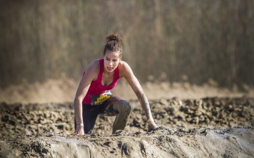 Woman climbing over a mud wall in an obstacle course 