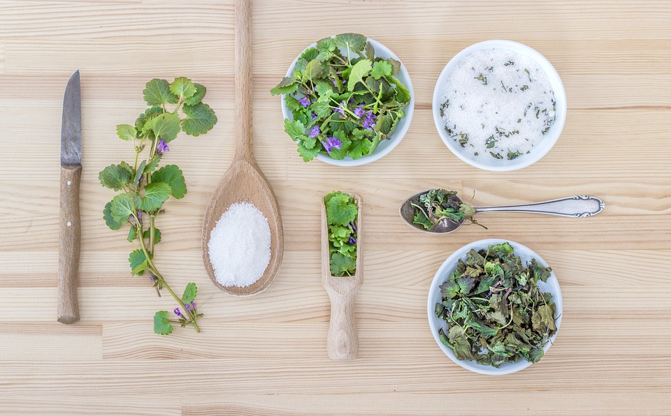 Herbs laid out on a cutting board and in small bowls with salt in small bowl and filling wooden spoon