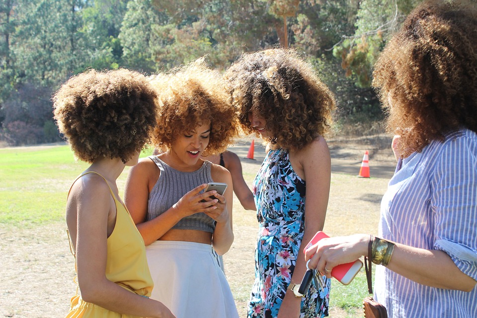 group of four women in park looking at phones