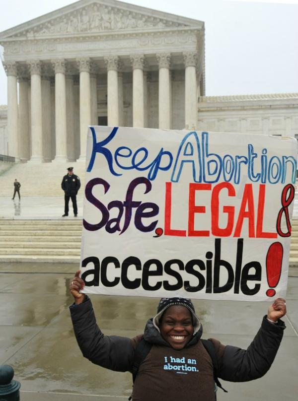 woman holding up poster that says "keep aborition safe, legal and accessible" and wearing a t-shirt that says "I had an abortion"