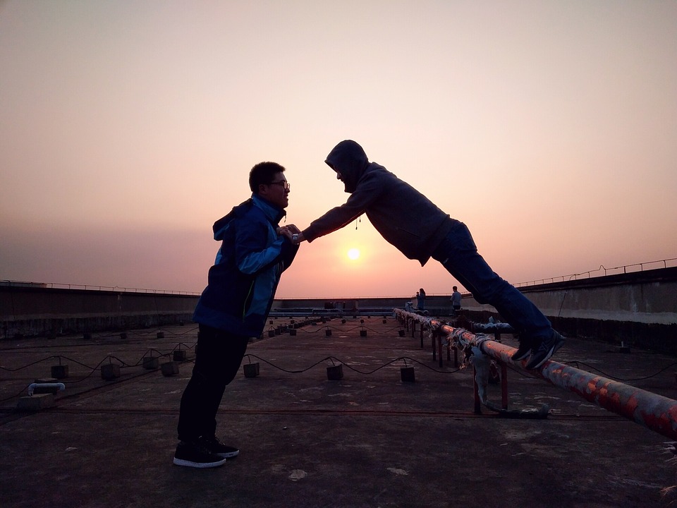 Two young men holding hands and balancing on a train track at sunset