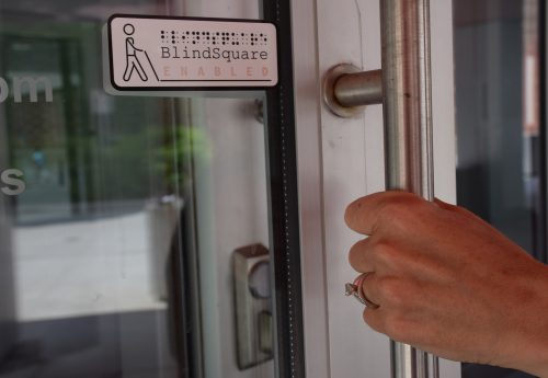 photo of BlindSquare sign on a glass door with a hand on the door handle