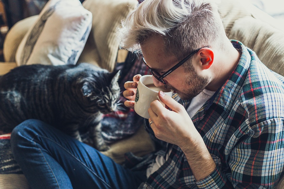 millennial sitting on sofa with cat, sipping a coffee
