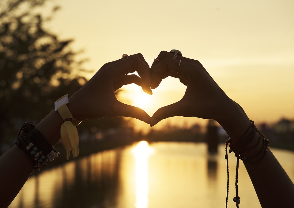 hands making heart shape in beach scene at sunset