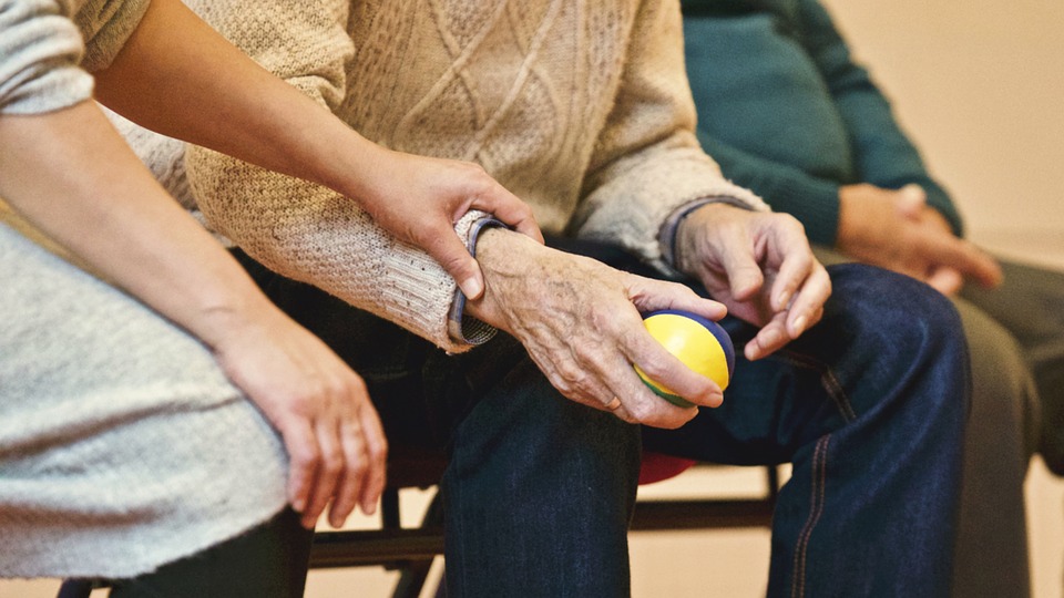 younger hands and older hands of people sitting on a bench. elderly man holding a ball