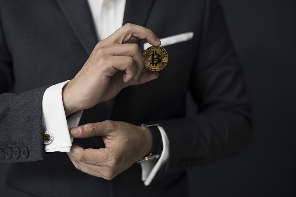 man in suit holding a bitcoin in his fingers