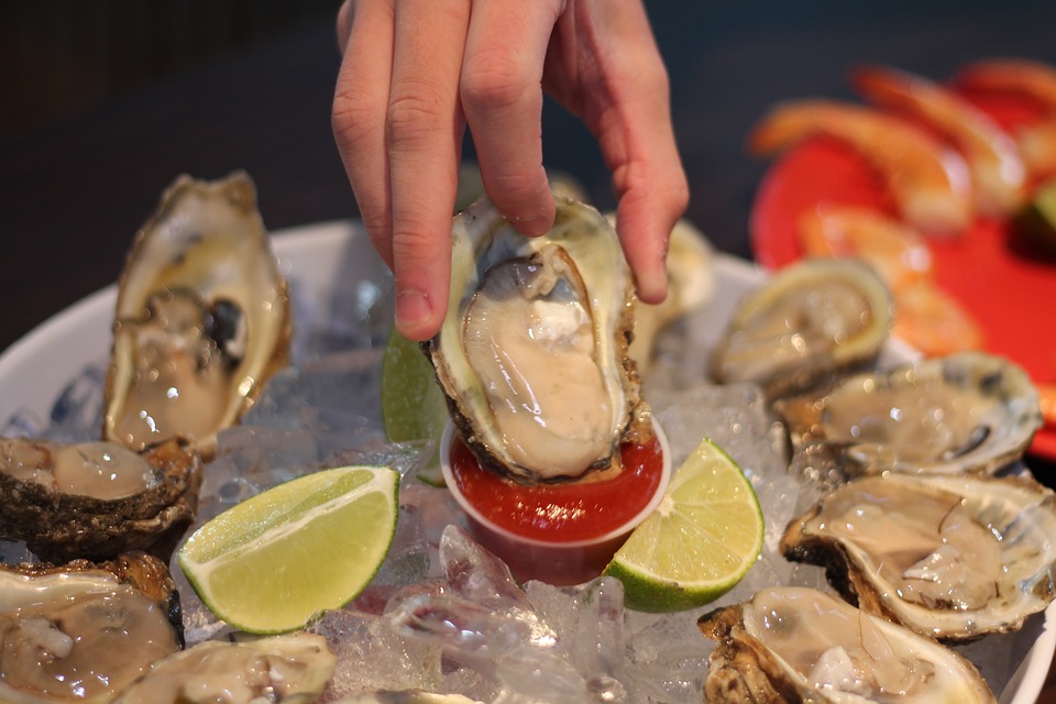 Hand of person dipping raw oyster into red sauce 