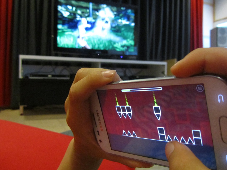 kids hands on phone playing video game with massive TV screen in background