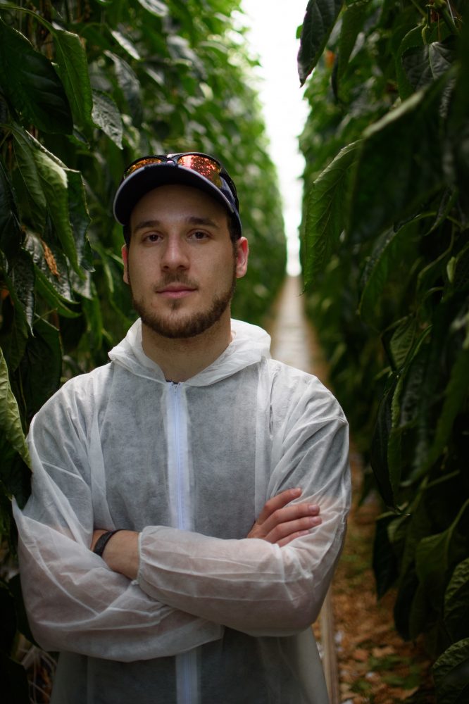 Dylan Sher, arms crossed, wearing baseball cap standing in tractor bay