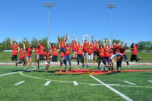 students jumping in the air on foodball field, wearing U of G logo tee shirts
