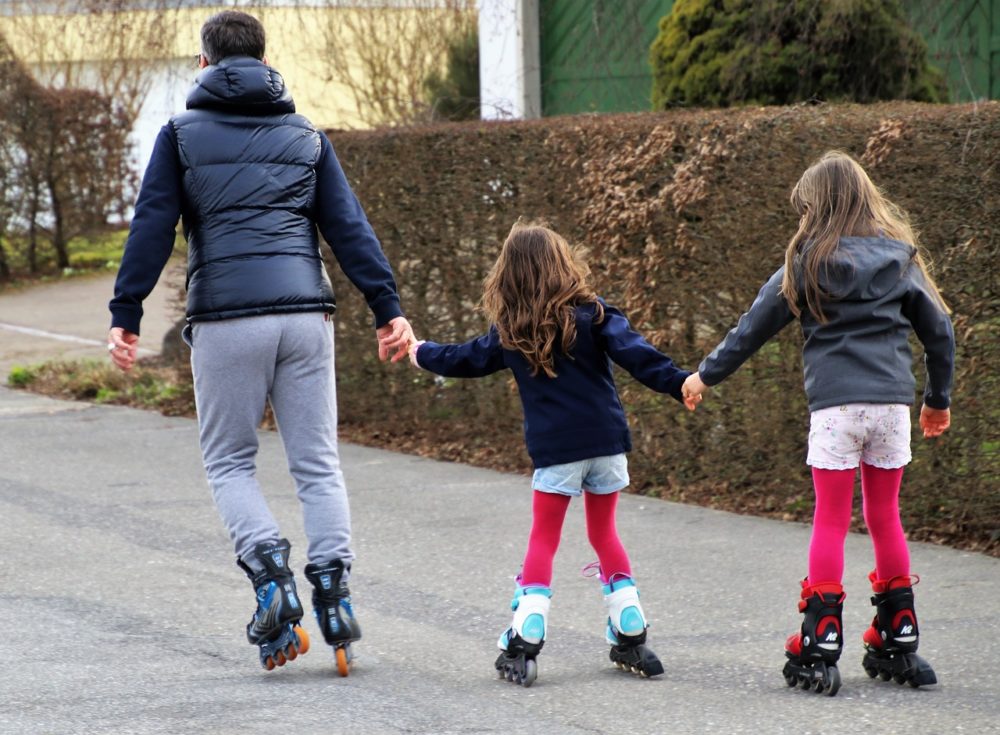 A dad and two daughters roller blading