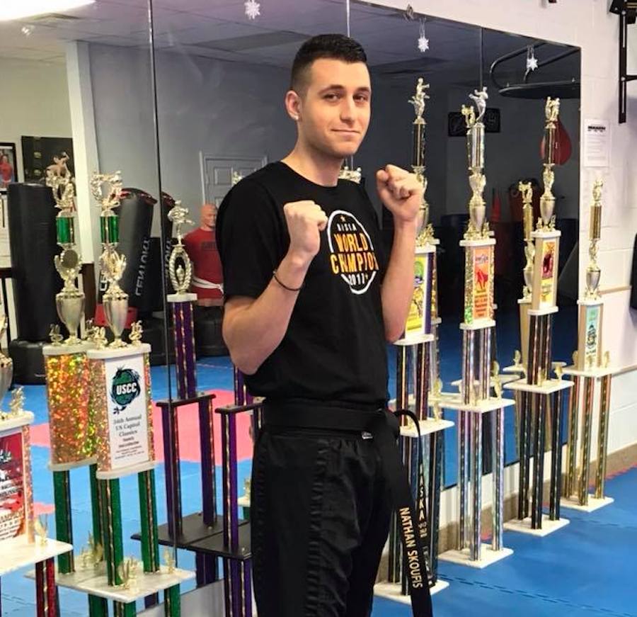 Martial artist with raised fists in front of row of trophies.