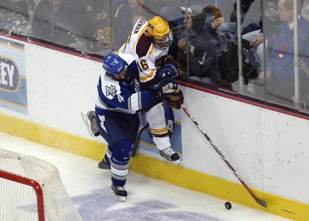 A hockey player forces another against the boards