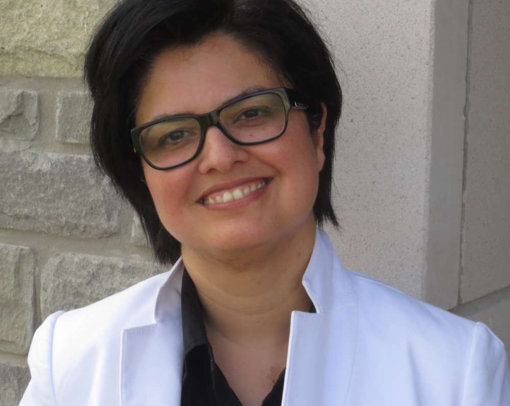 Dr. Rozita Dara smiles for a photo in front a stone brick building