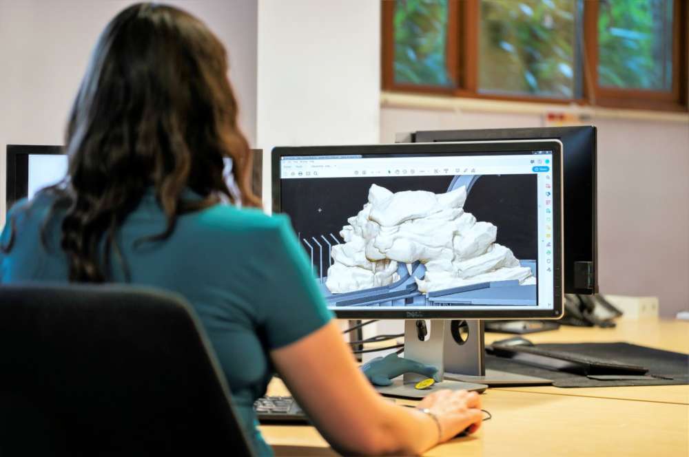a woman sits at a computer doing 3D modelling