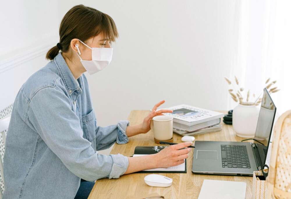 A woman in a mask works at a laptop