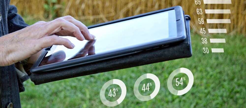 A researcher uses an iPad near a grain field