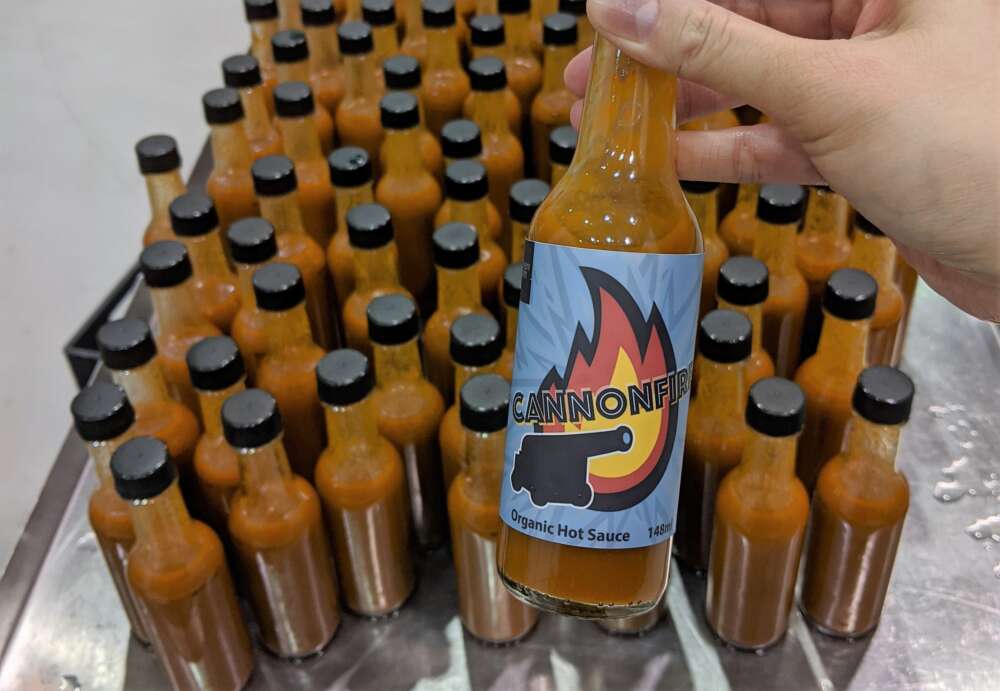 A hand holds a bottle with the Cannon Fire label hot sauce 