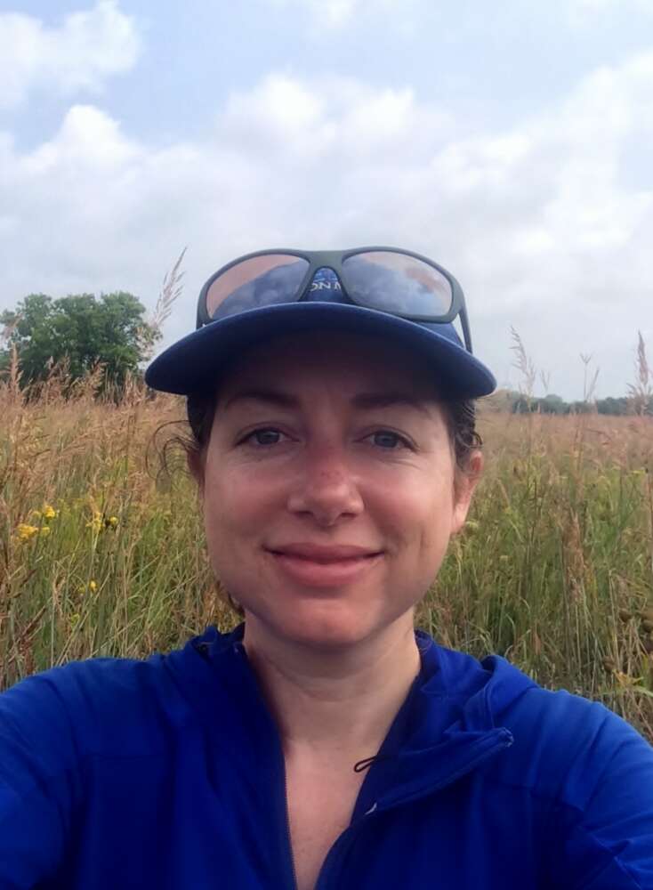 Closeup of woman in a field, wearing a brimmed hat and a blue top