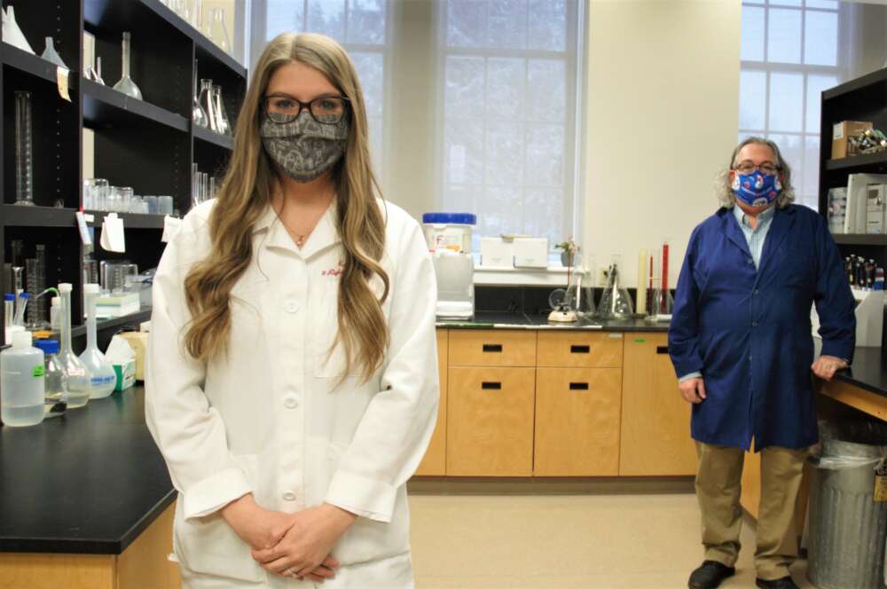 Two people stand in a lab, woman in front, man behind