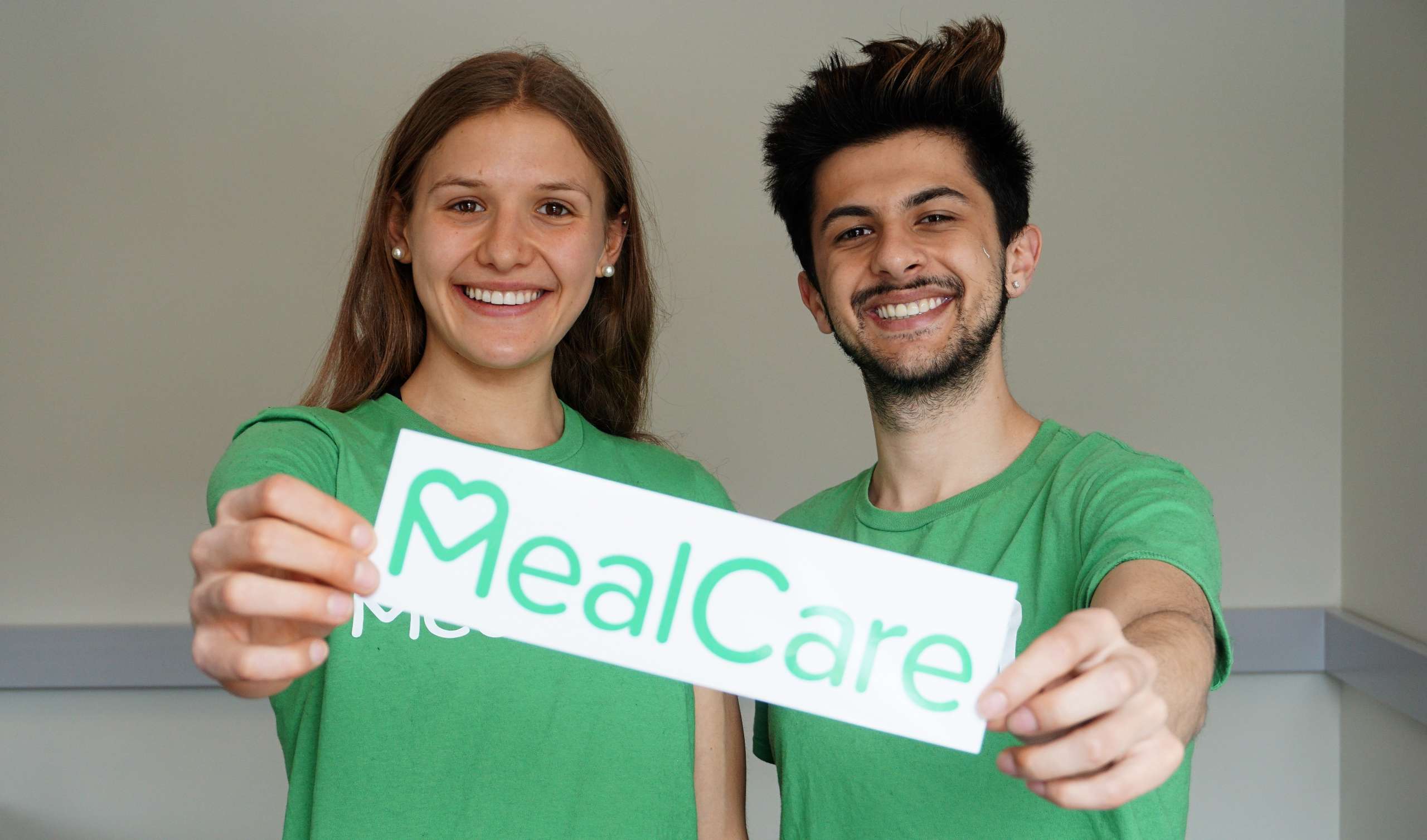 A woman and a man wearing matching gree nshirts hold a sign that reads MealCare