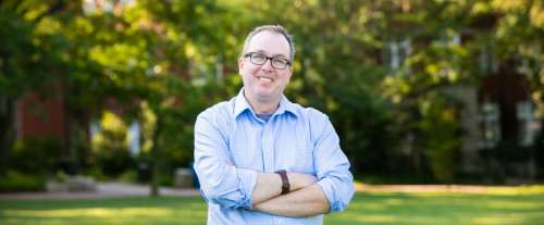 image of Dr. Andrew Bailey, smiling with his arms crossed at his chest, trees and grass in the background