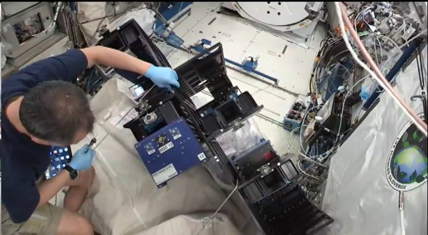An astronaut on the ISS uses tools to place carrier on a transfer try