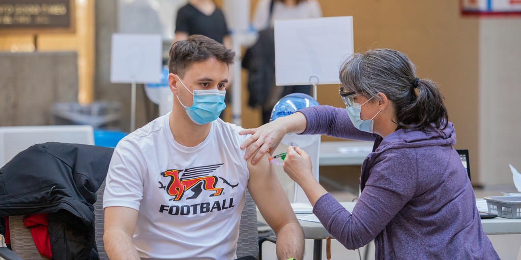 A person wearing Guelph Gryphon T-shirt gets a vaccine in the COVID-19 vaccination clinic in the University Centre on the U of G campus
