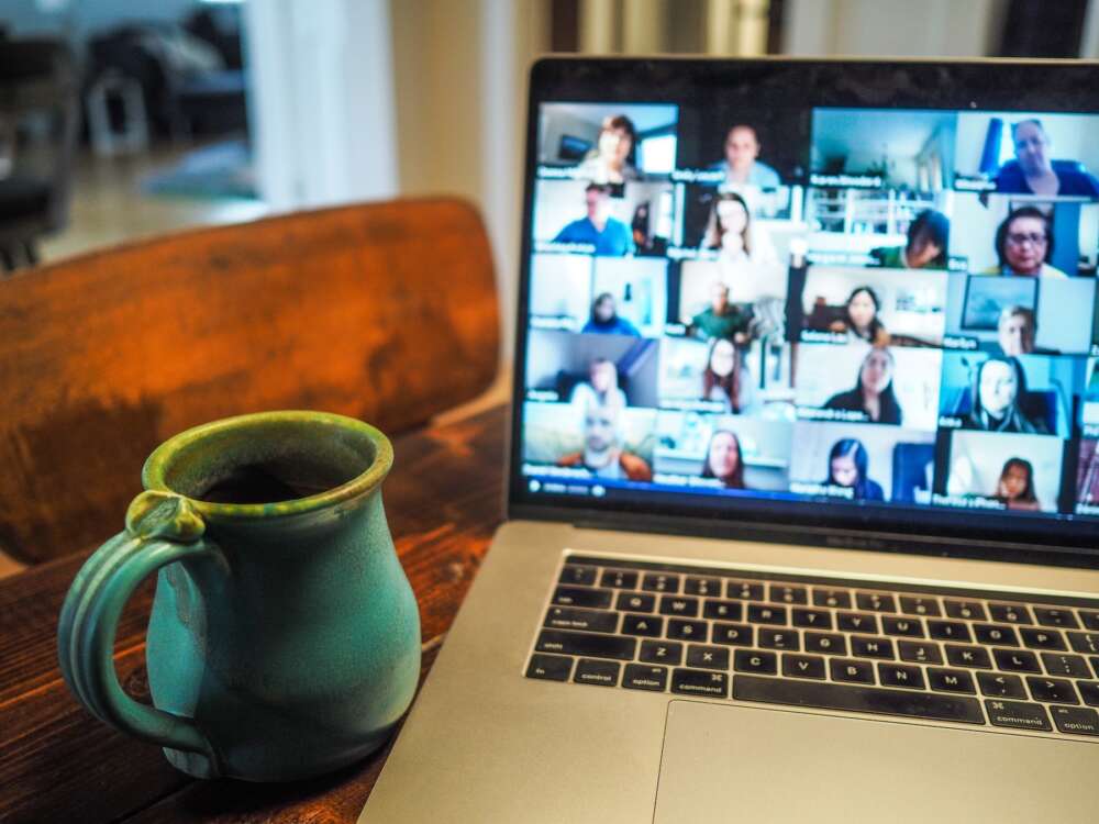 A ceramic mug sits beside a laptop with an online meeting on the screen
