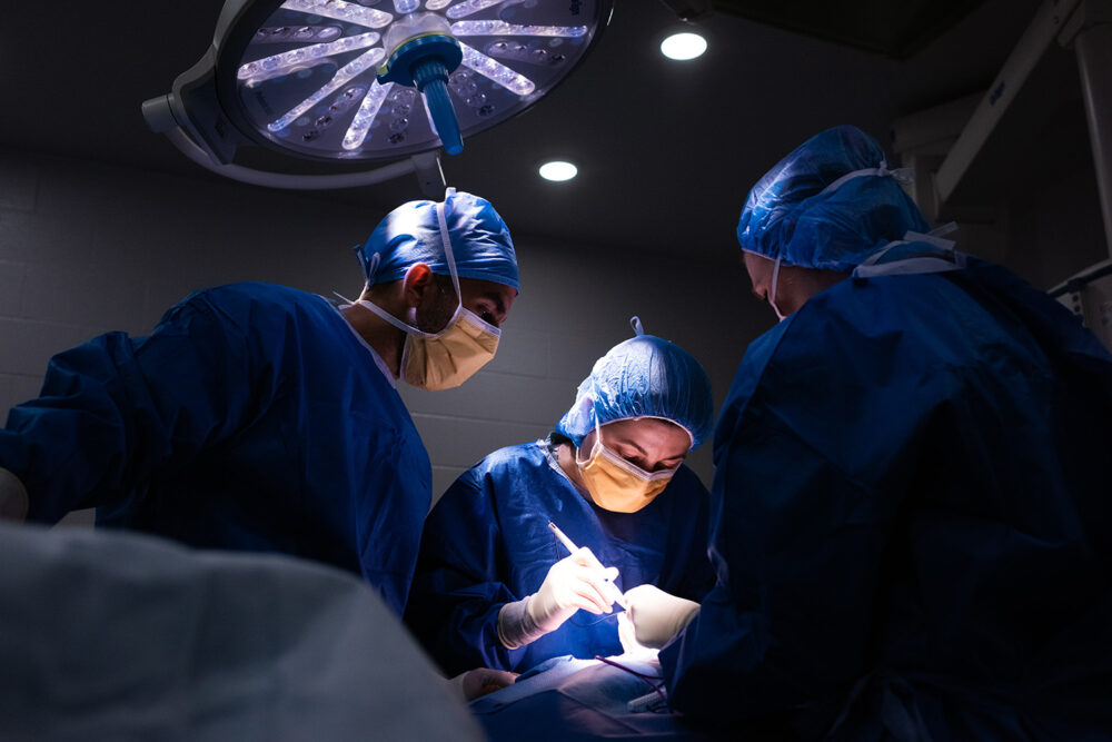 Three health care workers assist a surgery