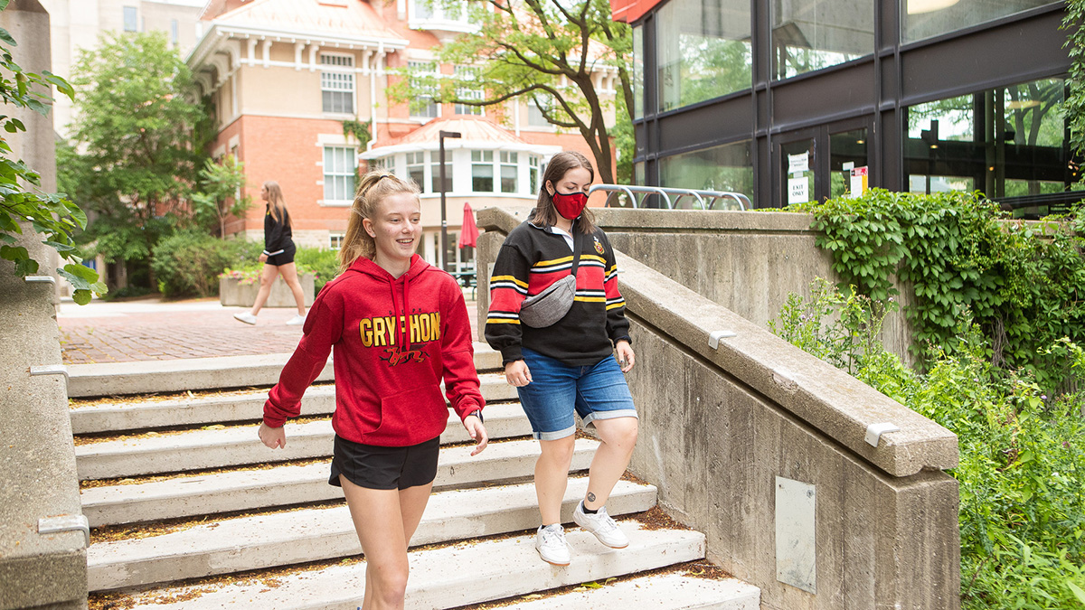 Two students wearing Gryphon sweaters walk down stairs on campus