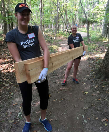 Two Project Serve volunteers carry 2x8 pieces of lumber