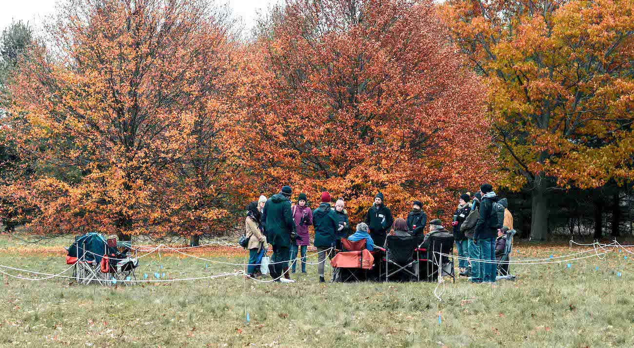 More than a dozen community members stand on an Arboretum field amid colourful autumn trees