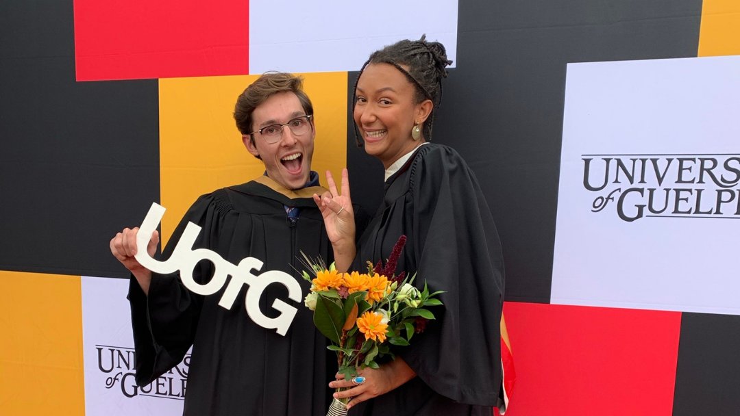 Two graduates wearing regalia smile for the camera