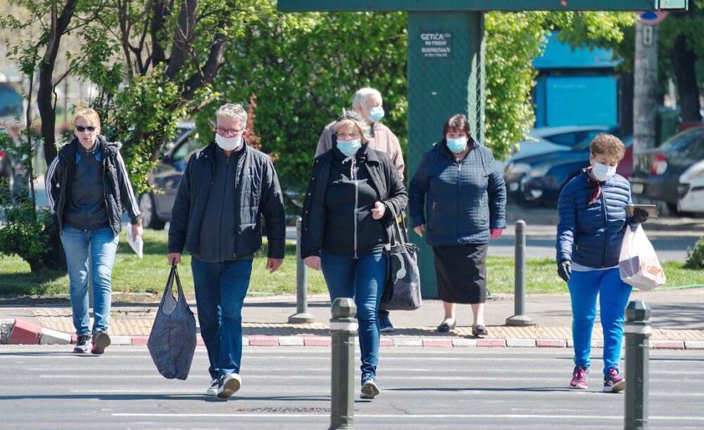 Six people wearing face masks are shown walking across a crosswalk