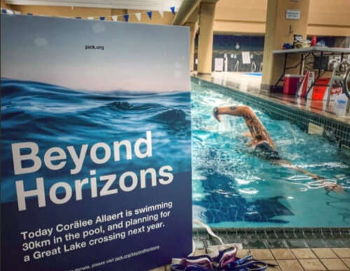 a sign reading 'Beyond Horizons' on a pool deck as Allert swims front crawl
