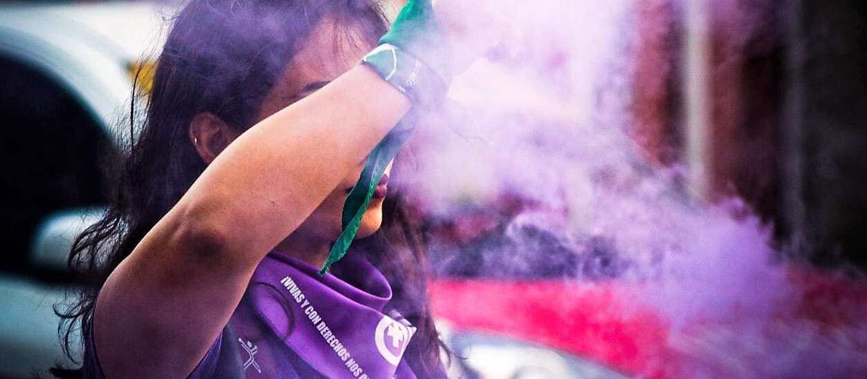 A woman wearing purple holds up her arm amid purple smoke