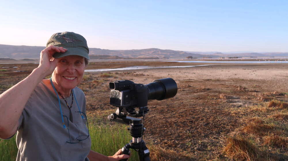 Roberta Bonday stands with a camera on a tripod on a sunny plain in Tanzania