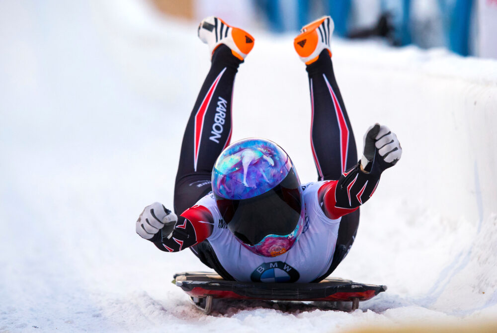 an athlete wearing a helmet raises their hands in victory while on a skeleton sled