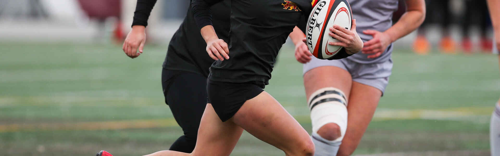 University of Guelph's Talia Hoffman sports a black uniform and holds a white, black, and red rugby ball during a game.