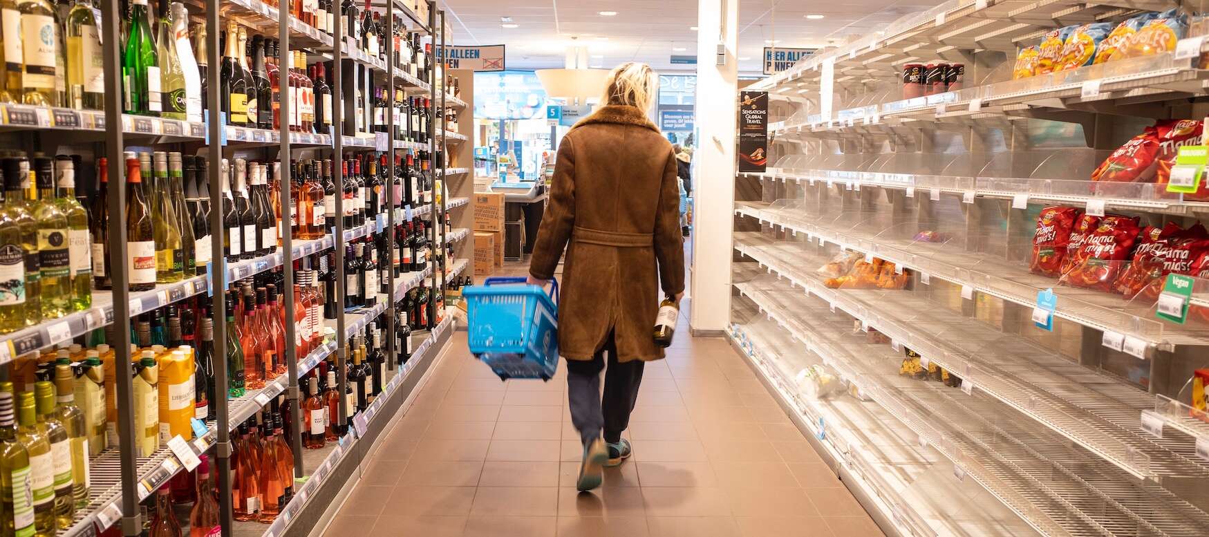 A person is seen from behind in a grocery store aisle with some empty shelves
