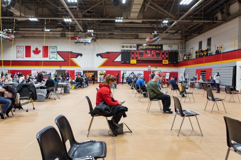 People sit on chairs while resting after vaccination in the Mitchell gym