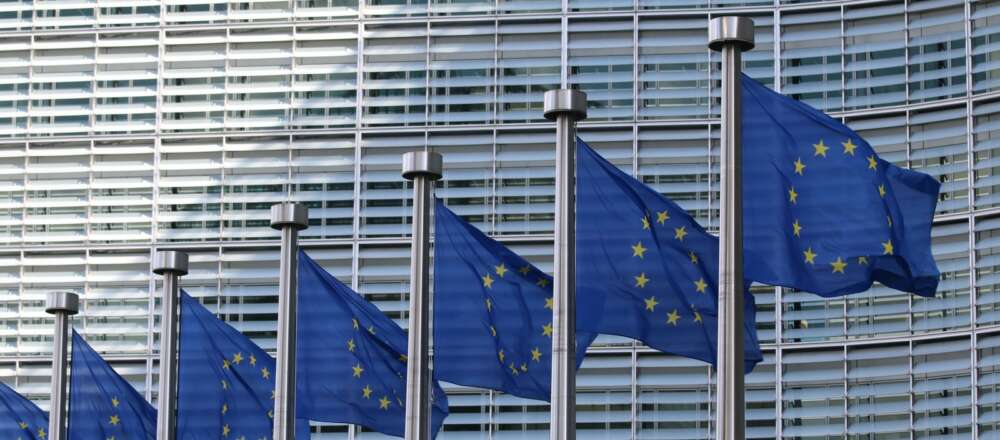 European Union (EU) flags (blue with yellow stars in a circle in the centre) fly in front of an office building.