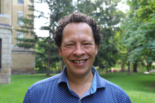 Lawrence Hill stands outside against stone building and trees