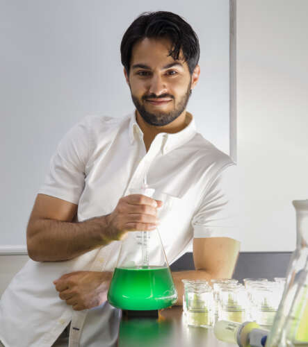 a man leans against a lab table holding a beaker of green fluid