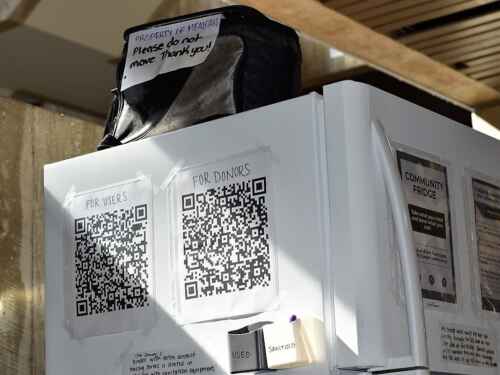 Two large QR codes are printed and taped to the side of a white fridge