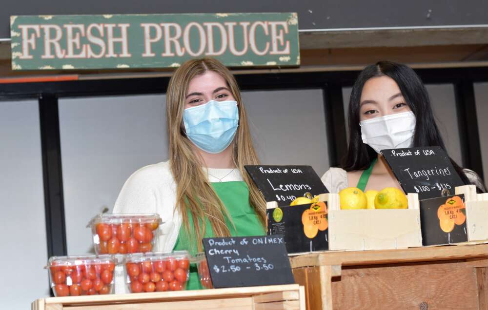 Food market organizers Maya Nickle and Vivian Ma stand behind crates of cherry tomatoes and lemons