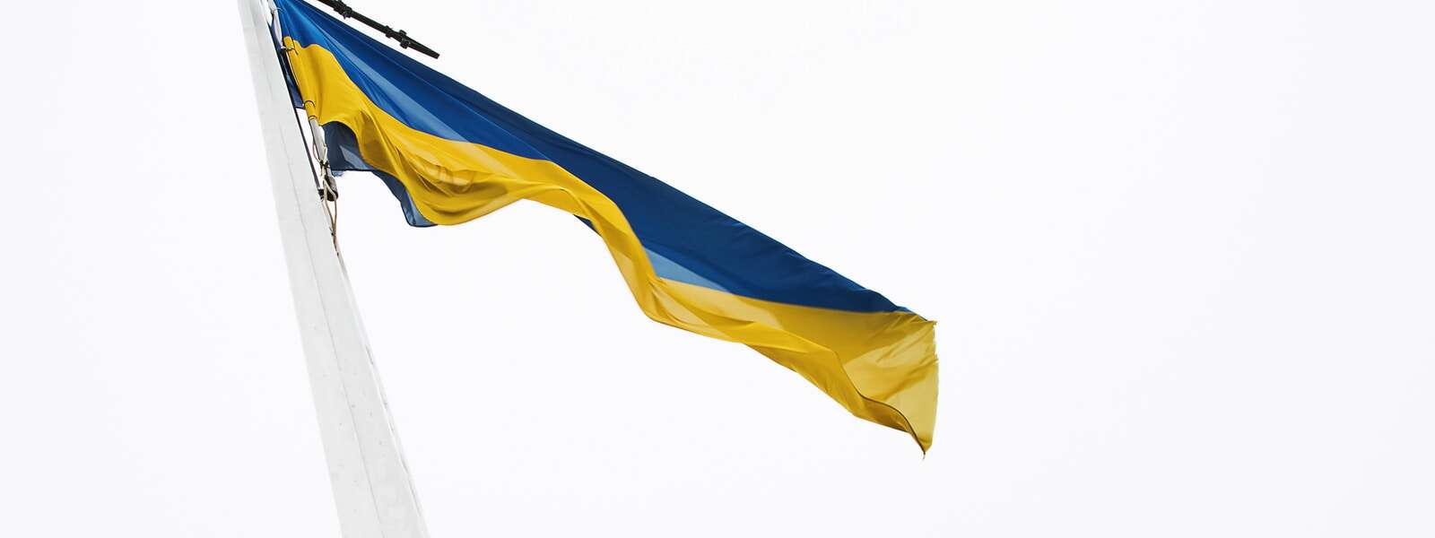 The Ukrainian flag (top half blue, bottom half yellow) flies against a white overcast sky.
