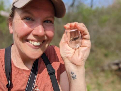 A closeup of a smiling Jessica Linton holding a mottled duskywing in a small jar