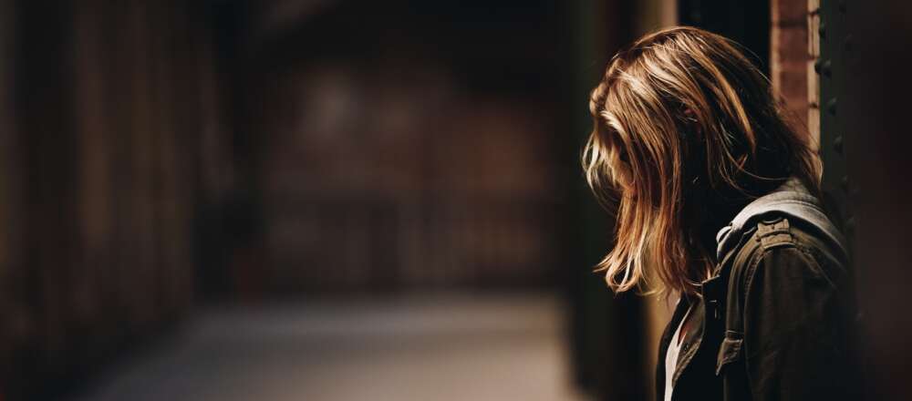 A person leaning against a wall in dim hallway